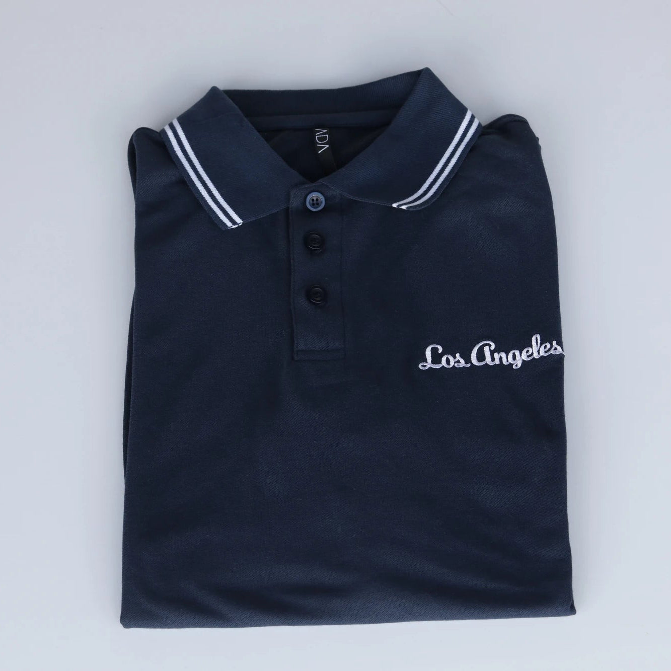 Folded navy blue polo shirt with 'Los Angeles' text on a light gray background